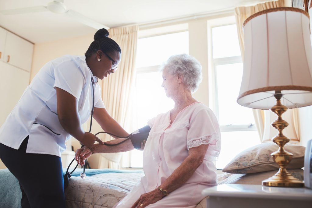 shutterstock_497636569-min Zorgmedewerker meet de bloeddruk van een oudere vrouw in een kamer.